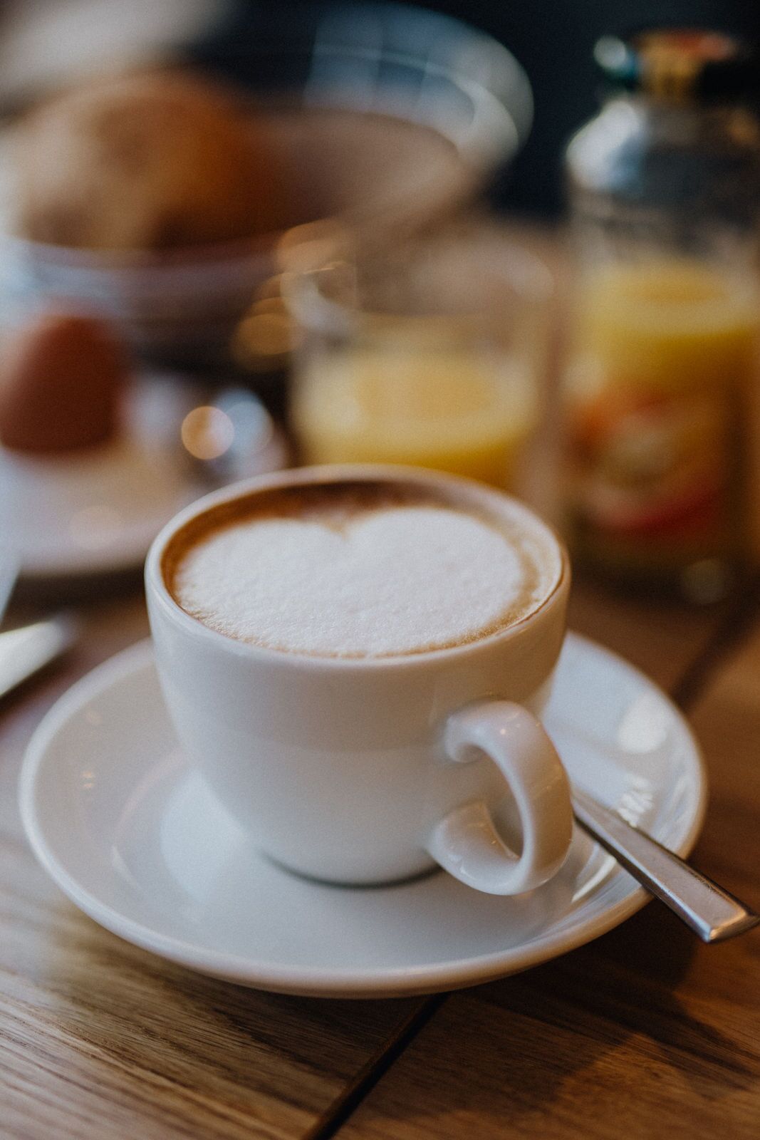 Uma xícara de café com desenho de coração no creme, apoiada em um tampo de mesa de madeira.