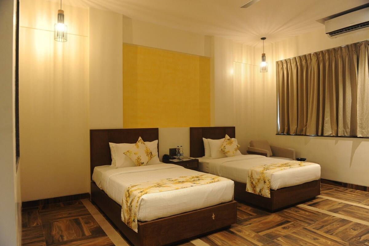 A hotel room with two beds, a wooden floor, a large window with curtains, and a ceiling fan.