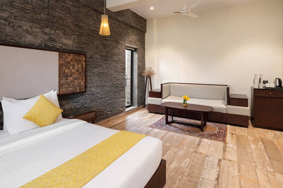 A modern hotel room with a large bed, a sofa, a coffee table, and a stone accent wall.