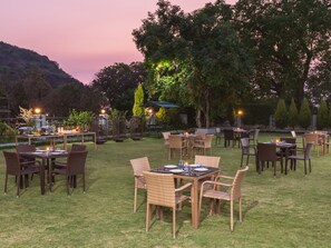 An outdoor dining area with tables and chairs, surrounded by trees and a view of hills. - The Summer House, Pachmarhi - AM Hotel Kollection (Pipariya)