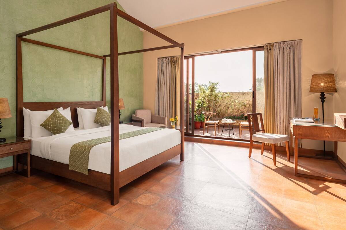 A spacious bedroom with a four-poster bed, a desk with a chair, and a balcony with potted plants.