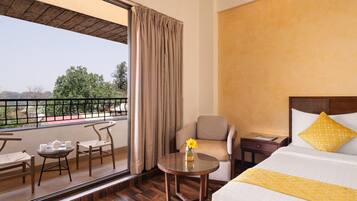 A hotel room with a balcony, a bed, a chair, a table, and a nightstand.