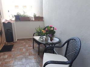 A small balcony with a tiled floor, a table with a vase of flowers, a chair, and potted plants. - B&B Da Andreina (Guspini)