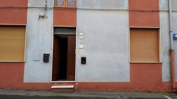 Un edificio con fachada roja y gris, una puerta visible y un escalón pequeño que lleva a la entrada.