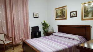 A bedroom with a bed, a desk, a chair, a plant, and three framed pictures on the wall. - B&B Da Andreina (Guspini)