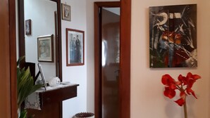 A hallway with a wooden door frame, a mirror, framed pictures, a vase, and a potted plant. - B&B Da Andreina (Guspini)