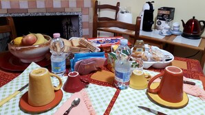 A dining table with various food items, a bowl of fruit, and a red kettle. - B&B Da Andreina (Guspini)