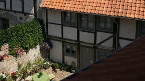 A traditional half-timbered house with a red-tiled roof and a small garden area with potted plants and a table. - Appartments Tilia (Quedlinburg)