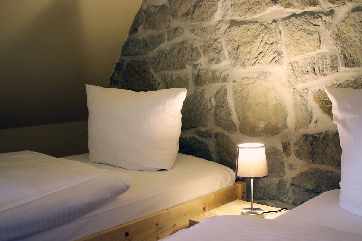Ein Schlafzimmer mit zwei Betten, einer Steinwand und einer Nachttischlampe.