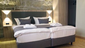 A modern bedroom with a large bed, two bedside tables, and a stone wall. - Appartments Tilia (Quedlinburg)