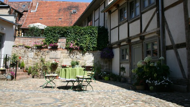 A courtyard with a stone floor, a table with chairs, and potted plants. - Appartments Tilia (Quedlinburg)