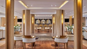 Un hall d’hôtel moderne avec des piliers en bois, des espaces aménagés pour s’asseoir et un bar en arrière-plan.