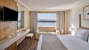 Une chambre d’hôtel avec un grand lit, un téléviseur fixé au mur, un canapé, un bureau et une vue sur un lac.