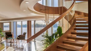 Un intérieur moderne avec un escalier en colimaçon, de grandes fenêtres et un coin salon offrant une vue sur l’eau.