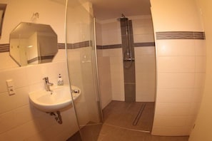 A bathroom with a sink, mirror, shower, and tiled walls.