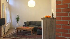 Un salon chaleureux avec un canapé, une table basse, une plante en pot et un luminaire suspendu.