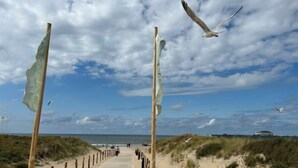 Ein Promenadweg am Strand mit Holzpfählen und blauem Himmel.