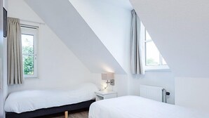 Ein modernes Schlafzimmer mit zwei Betten, einem Nachttisch, einer Lampe und einem Fenster mit Vorhängen.