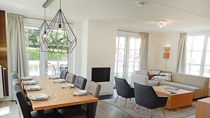 Ein modernes Wohnzimmer mit Essbereich, großen Fenstern, einem Flachbildfernseher und einer Couch.