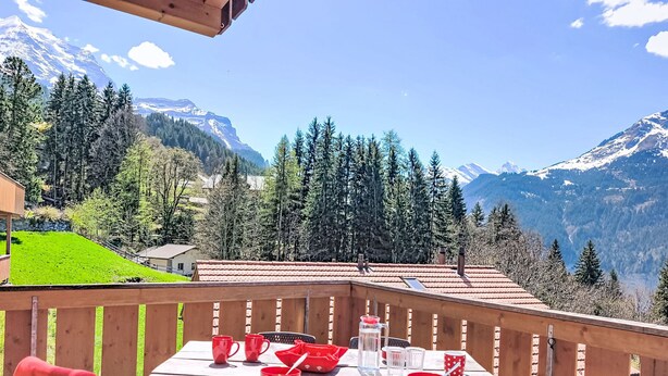 Eine Holzterrasse mit Essplatz, mit Blick auf eine gebirgige Landschaft.