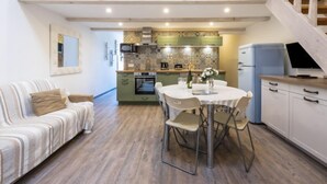 Un vaste espace de vie comprenant un canapé, une table à manger avec des chaises, une cuisine avec des meubles verts et un escalier menant à l’étage supérieur.