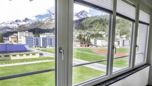 A room with a large window overlooking a sports field and buildings, with a mountain in the background. - Chesa Ova Cotschna 304 by Interhome (St. Moritz)