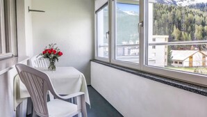 A balcony with a table and chairs, a vase with red flowers, and a view of a mountain and forest. - Chesa Ova Cotschna 304 by Interhome (St. Moritz)