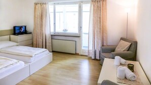 A hotel room with a bed, a TV, a window with curtains, a table with towels, and a chair. - Chesa Ova Cotschna 304 by Interhome (St. Moritz)