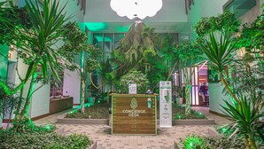 Un mostrador de conserjería en un vestíbulo con una exhibición de plantas tropicales y una lámpara grande con forma de nube.