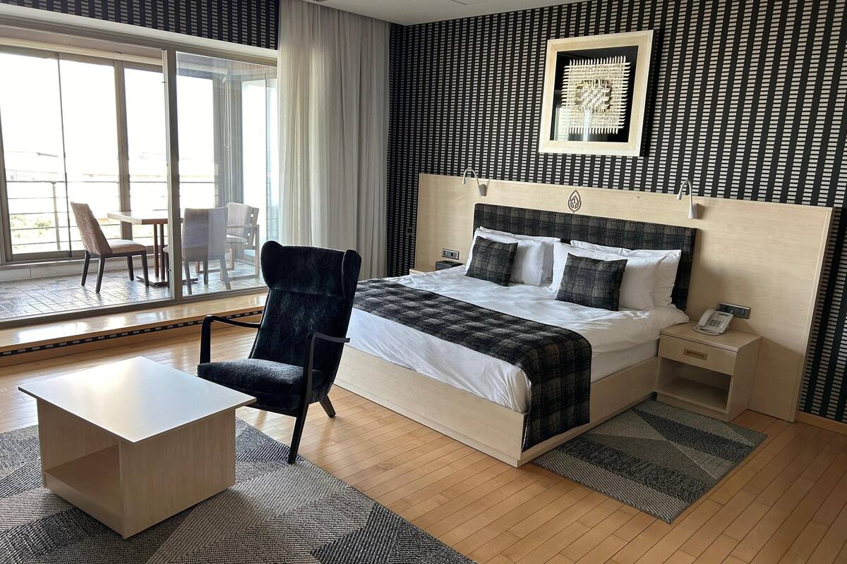 Une chambre d’hôtel équipée d’un lit, d’une table de chevet, d’une chaise et offrant une vue sur l’extérieur grâce à de grandes fenêtres.