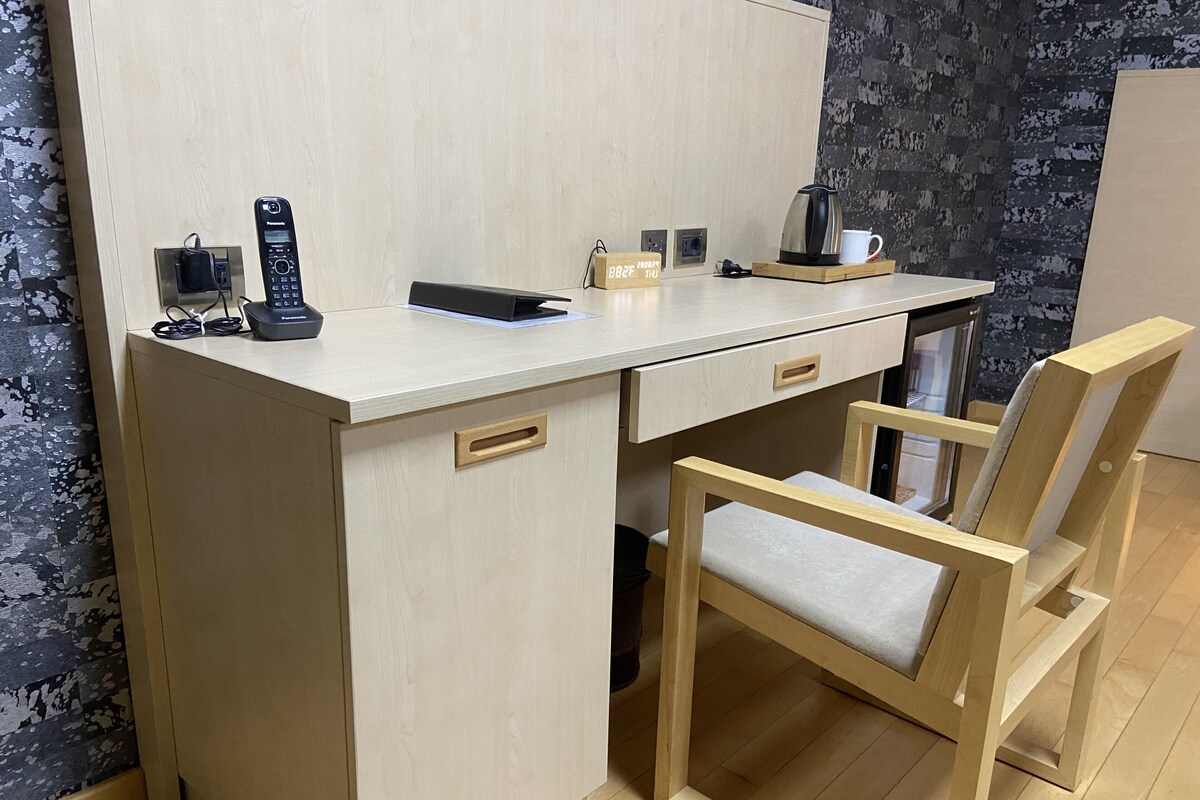 Een functionele, moderne werkruimte met een houten bureau, een stoel, een koffiezetapparaat en een stekkerdoos.