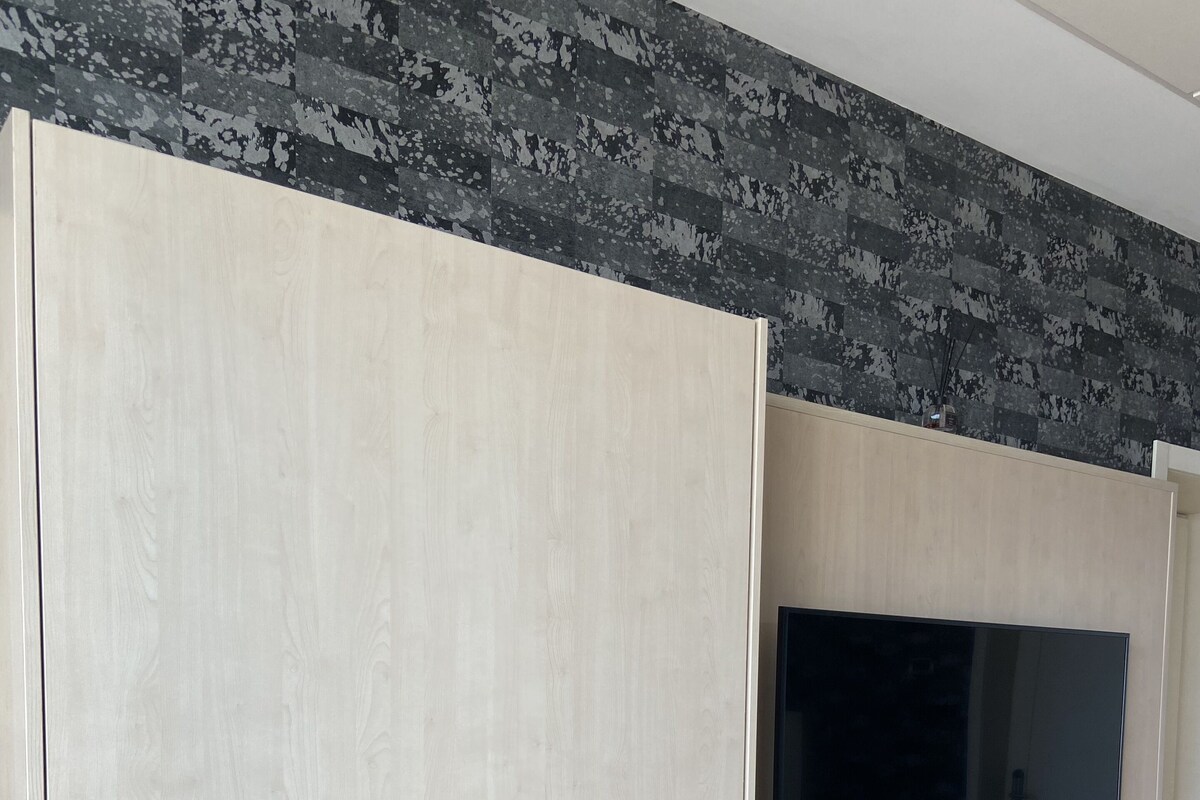 Een kamer met een grote garderobe, een wandgemonteerde flatscreen televisie en een klein houten plankje.