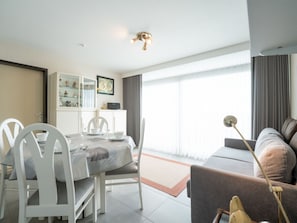 A modern living room with a dining area, a sofa, a lamp, and a view through large windows. - Astrid 704 with balcony by Interhome (Bredene)