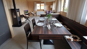 En moderne spisestue med et træbord dækket til seks personer, en pejs og et stort vindue med gardiner.