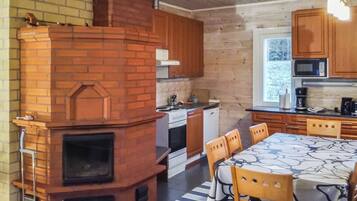 Une cuisine avec une cheminée en briques, des armoires en bois, une table à manger avec des chaises et une fenêtre.