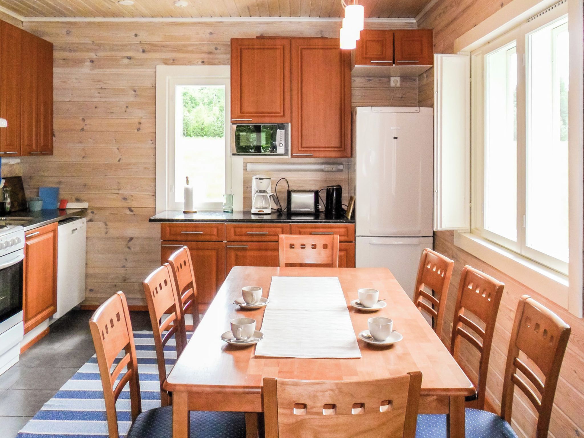 Cocina tipo cabaña de madera con una mesa de comedor para cuatro, equipada con electrodomésticos básicos como microondas, cafetera y refrigerador.