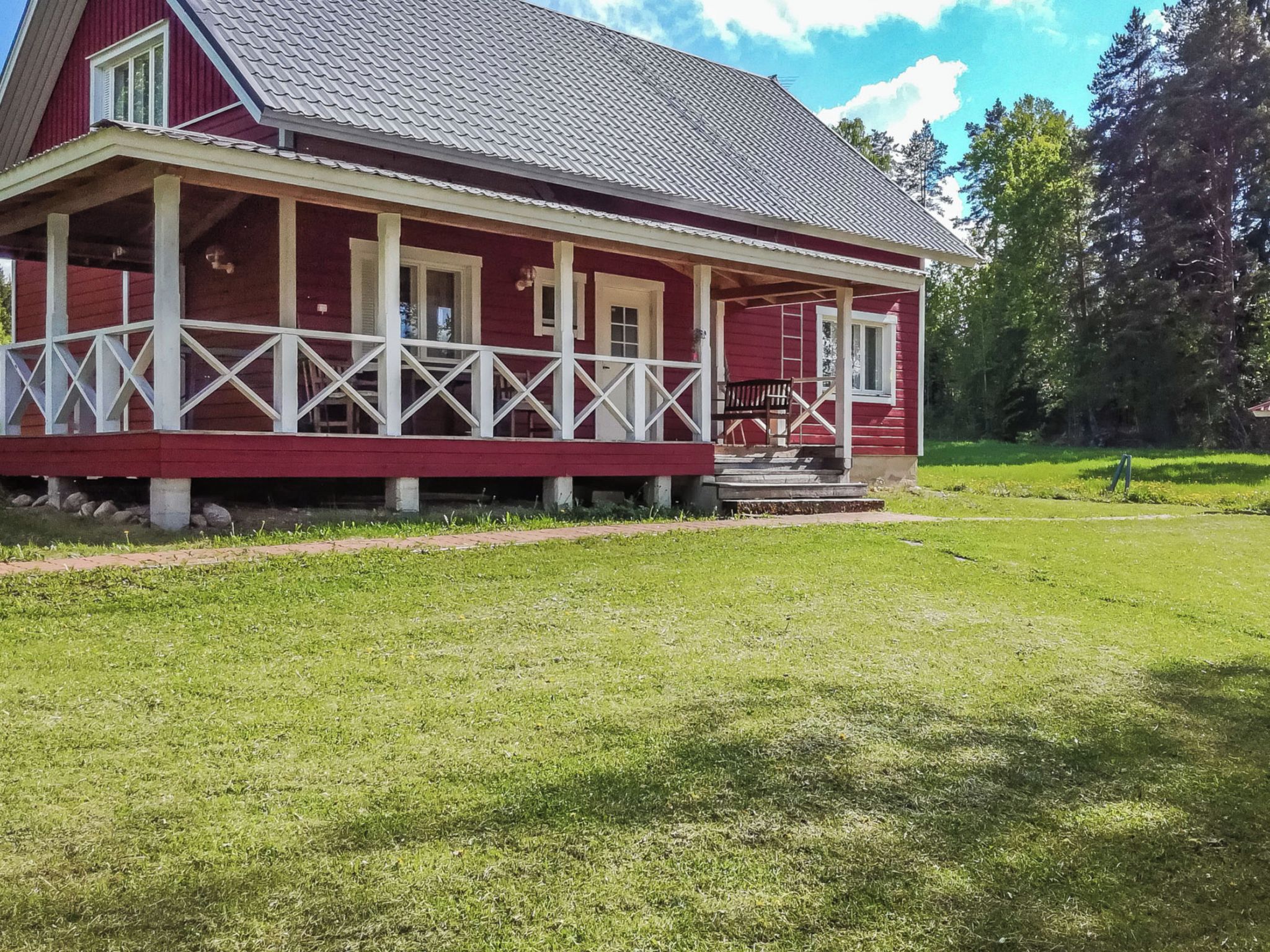 Een rode woning met een veranda en een gazon.