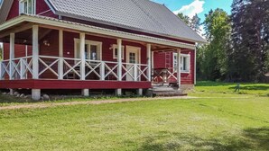 Una casa di legno rossa con un portico, un cortile con erba e alberi sullo sfondo.
