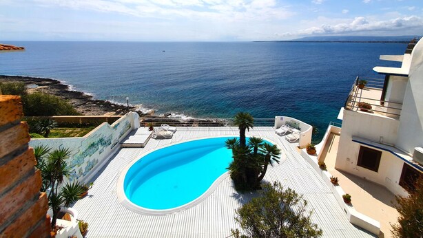 Une piscine sur le toit, offrant une vue sur la mer, et entourée d’immeubles et de palmiers.
