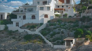 Un bâtiment situé sur la côte, doté de nombreux balcons, un sentier en pierre menant à une petite entrée et une rive rocheuse.