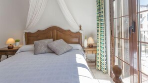 A neatly made bed with a wooden headboard, two bedside lamps, and a window with curtains. - Porto Fino by Interhome (Empuriabrava)