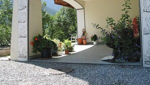 Eine überdachte Außenpatio-Terrasse mit Bergblick, umgeben von Kübelpflanzen und einer kleinen Statue.