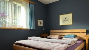 Ein Schlafzimmer mit Bett, Nachttisch, Lampe und einem Fenster mit Vorhängen.