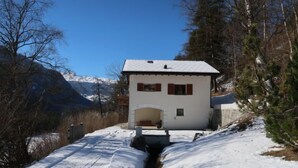 Ein weißes Gebäude mit einem geneigten Dach, einer kleinen Veranda und einem schneebedeckten Weg, der dorthin führt.