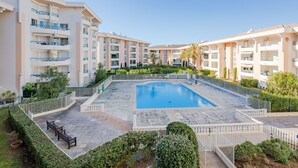 A hotel with a central swimming pool surrounded by a garden, multiple balconies, and a clear sky. - Apartment L'Open by Interhome (Fréjus)