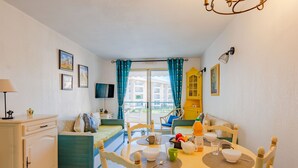A cozy room with a dining table, chairs, a sofa, a TV, and a balcony with blue curtains. - Apartment L'Open by Interhome (Fréjus)