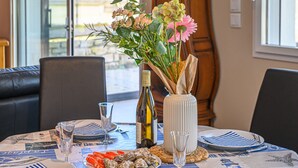 Een gedekte eettafel met borden, bestek en een fles wijn, plus een bloevas en een wijnglas op tafel.
