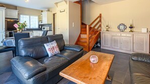 Een moderne woonkamer met een leren bank, een houten salontafel en een trap naar een keuken.