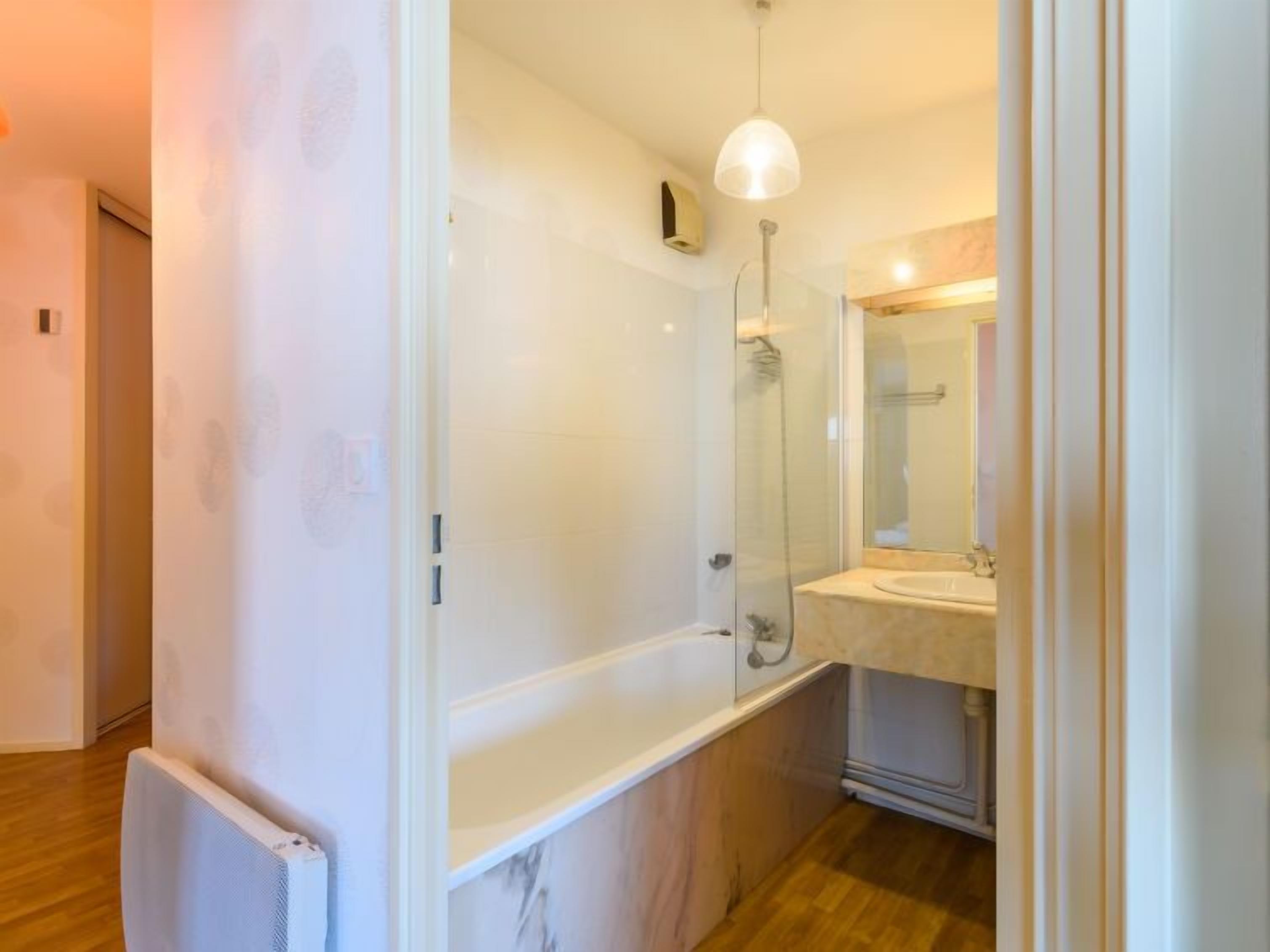 A modern bathroom with a glass shower enclosure, a marble-topped bathtub, and a sink with a mirror.