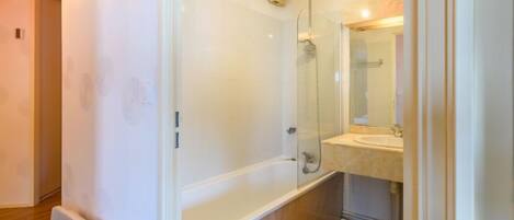 A modern bathroom with a glass shower enclosure, a marble-topped bathtub, and a sink with a mirror.